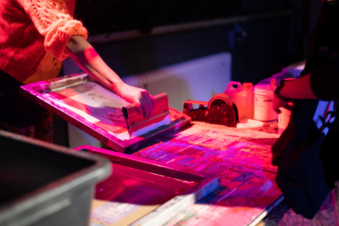 Tangan sedang mencetak dengan mesin silkscreen di bawah cahaya merah